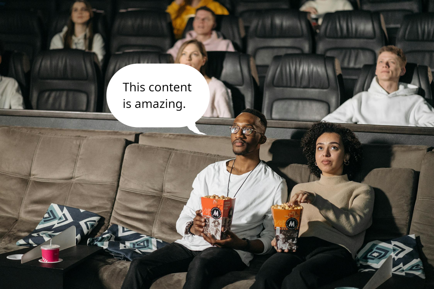 Two people sitting in a movie theater eating popcorn. A thought bubble appears above one person's head and it says 'This content is amazing'
